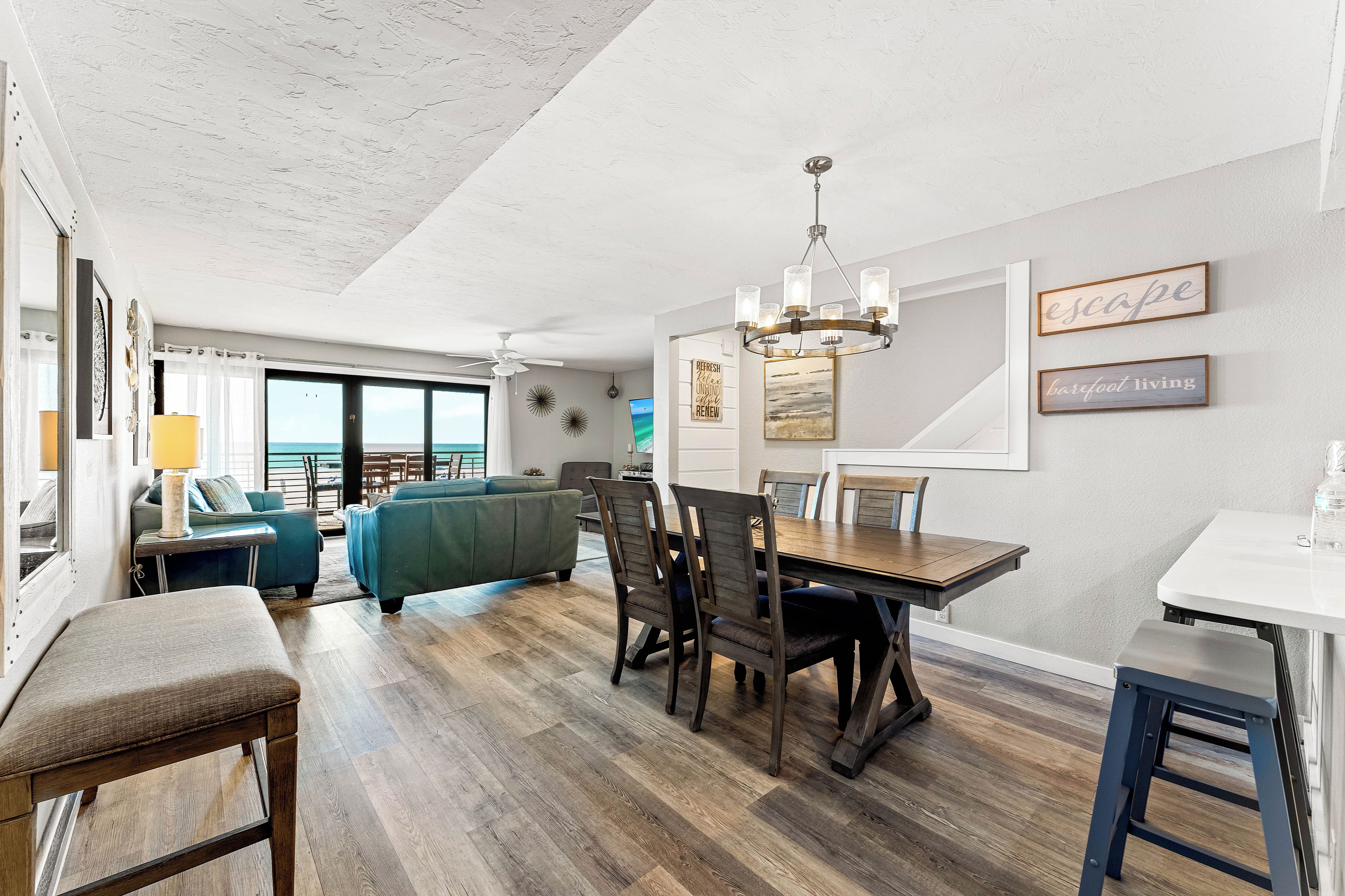 A spacious living area with a dining table, chairs, and a view of the ocean through large windows.
