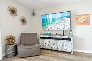 Una sala de estar con televisor, decoración en la pared, una silla y un mueble de madera.