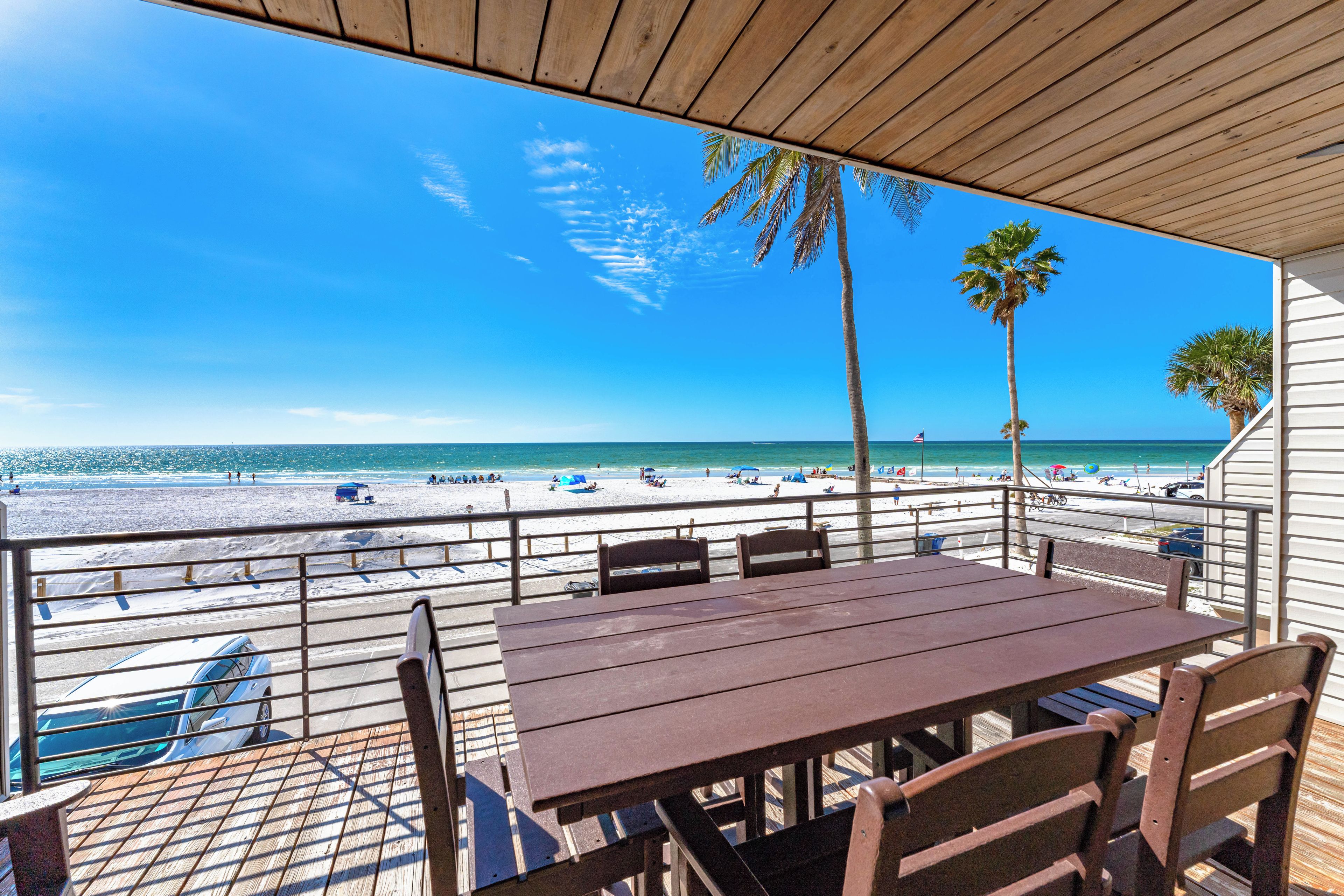 A beachside patio with a view of the ocean, a table, chairs, and a railing.