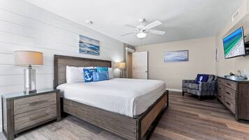 A bedroom with a bed, nightstands, a desk, a chair, a ceiling fan, and artwork on the walls.