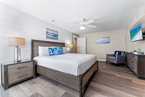 A bedroom with a bed, nightstands, a desk, a chair, a ceiling fan, and artwork on the walls. - Fanta-Sea on the Beach by Beachside Management - 55 Beach Rd (Siesta Key)