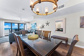 A spacious dining area with a large glass table, wooden chairs, and a modern chandelier. - Fanta-Sea on the Beach by Beachside Management - 55 Beach Rd (Siesta Key)