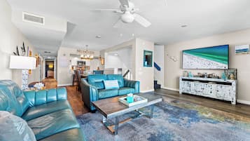 Uma sala de estar moderna com um sofá azul, uma mesa de centro, uma televisão e um quadro grande com uma cena de praia.