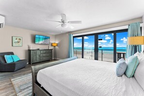 A bedroom with a large bed, a ceiling fan, a TV, a dresser, and a view of the ocean. - Fanta-Sea on the Beach by Beachside Management - 55 Beach Rd (Siesta Key)