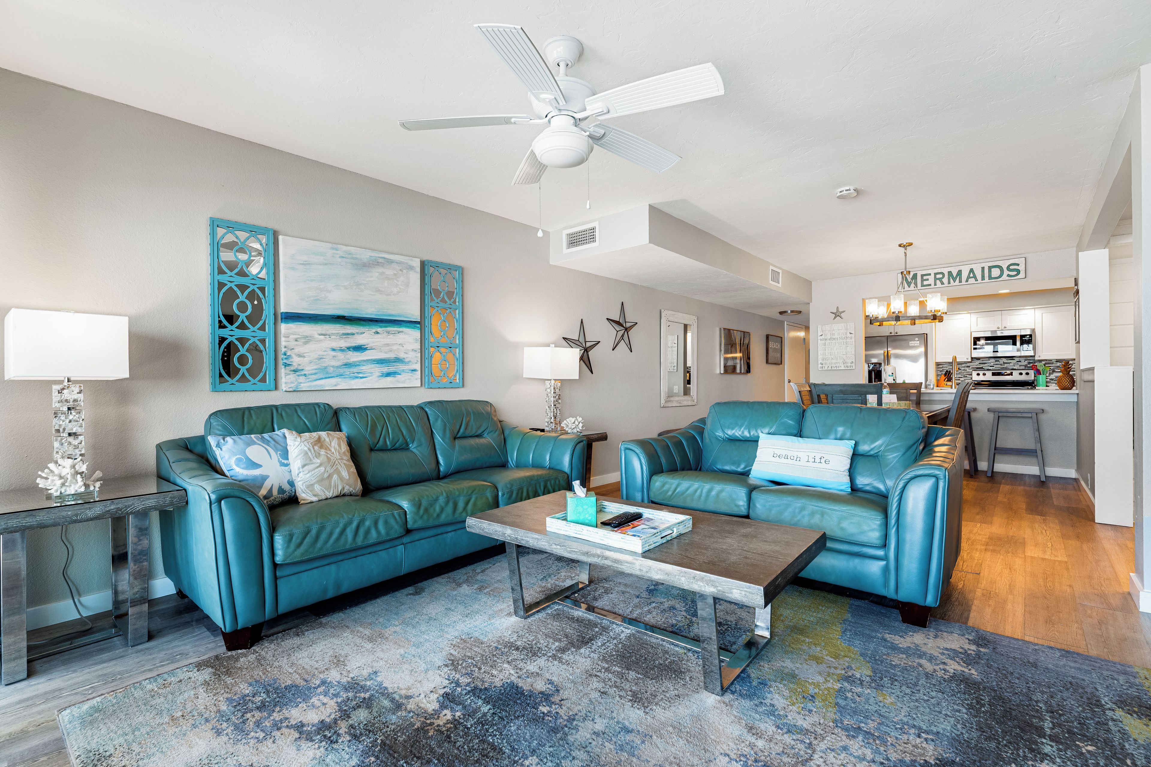 A living room with two teal leather sofas, a coffee table, and a ceiling fan.