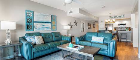A living room with two teal leather sofas, a coffee table, and a ceiling fan.