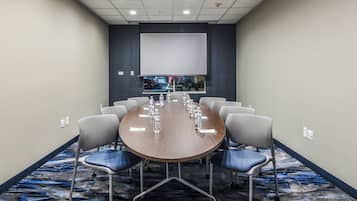 Un salón de conferencias con una gran mesa ovalada, seis sillas y una pantalla de proyector.