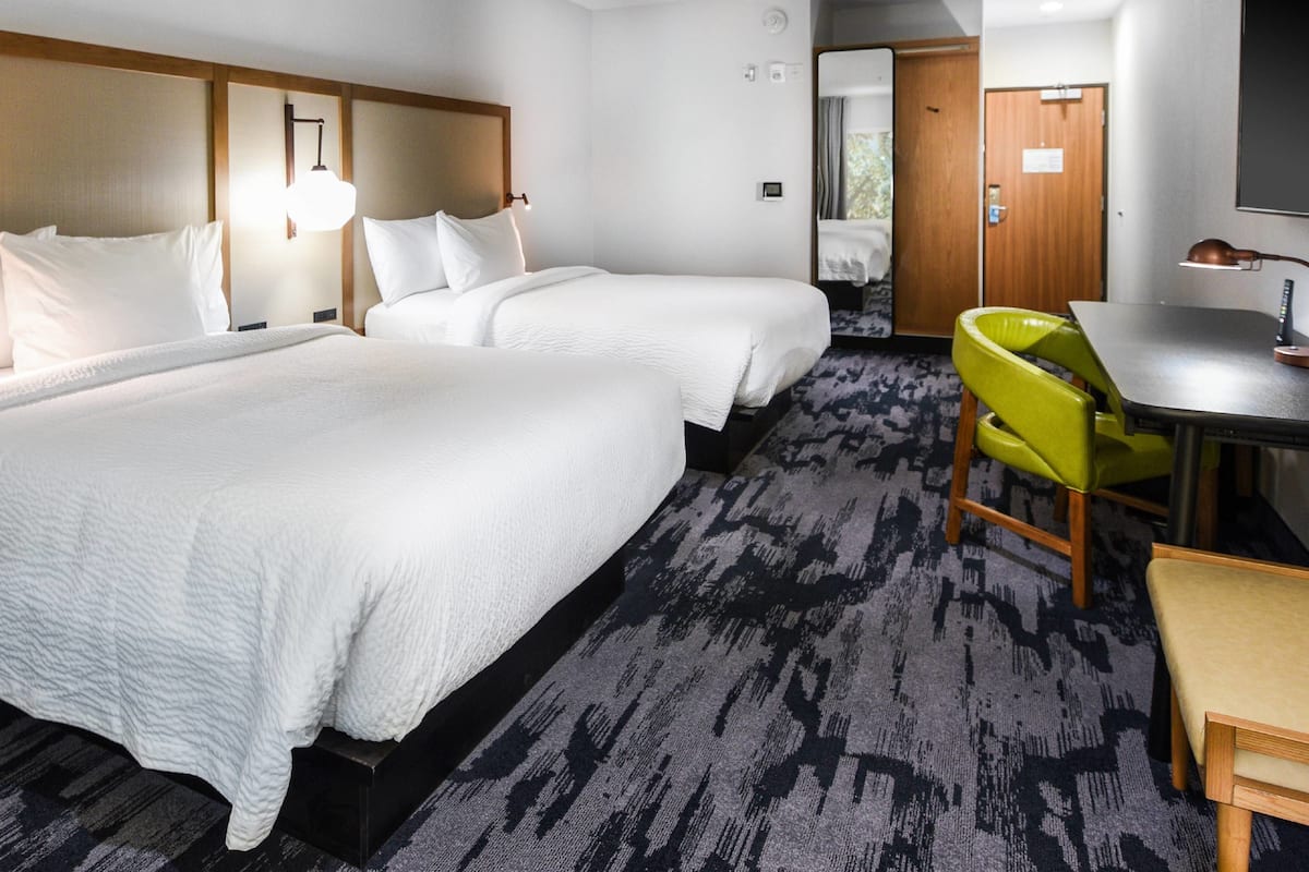 A hotel room with two beds, a desk, and a chair.