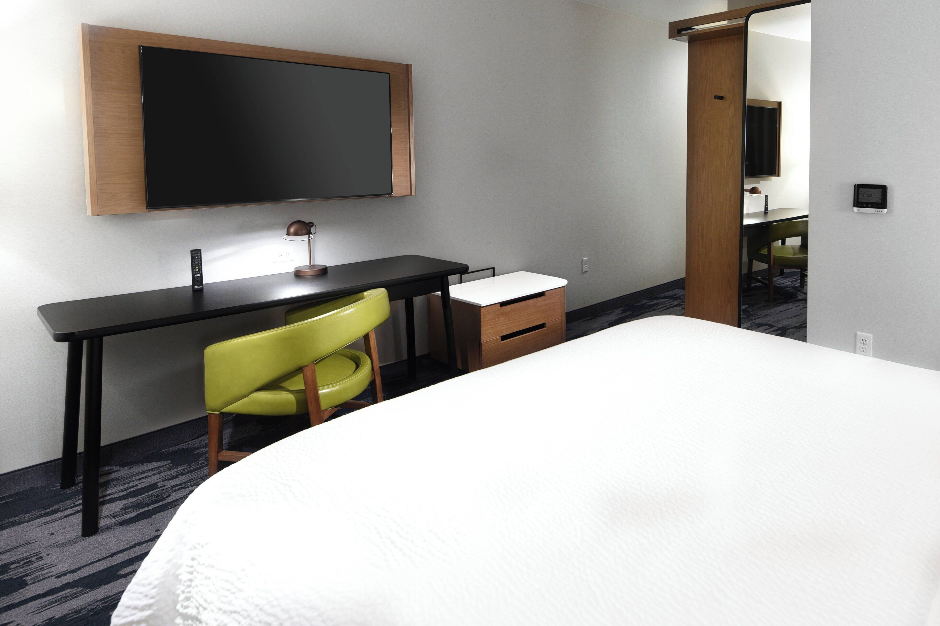 Ein Hotelzimmer mit einem Bett, einem Schreibtisch, einem Stuhl, einem Flachbildfernseher und einem kleinen Schrank.
