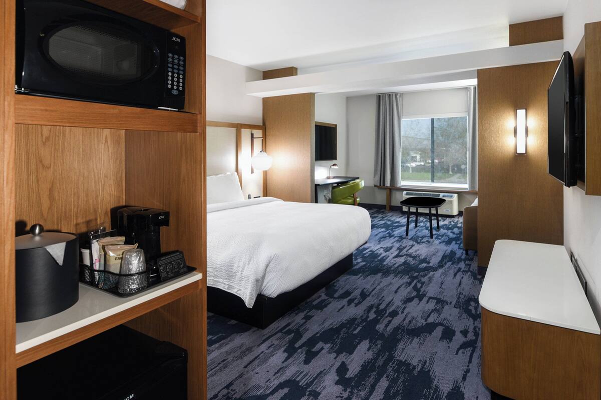 A hotel room with a bed, a desk with a microwave, a coffee maker, and a TV.