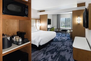 Habitación de hotel con una cama, un escritorio con microondas, cafetera y televisión.
