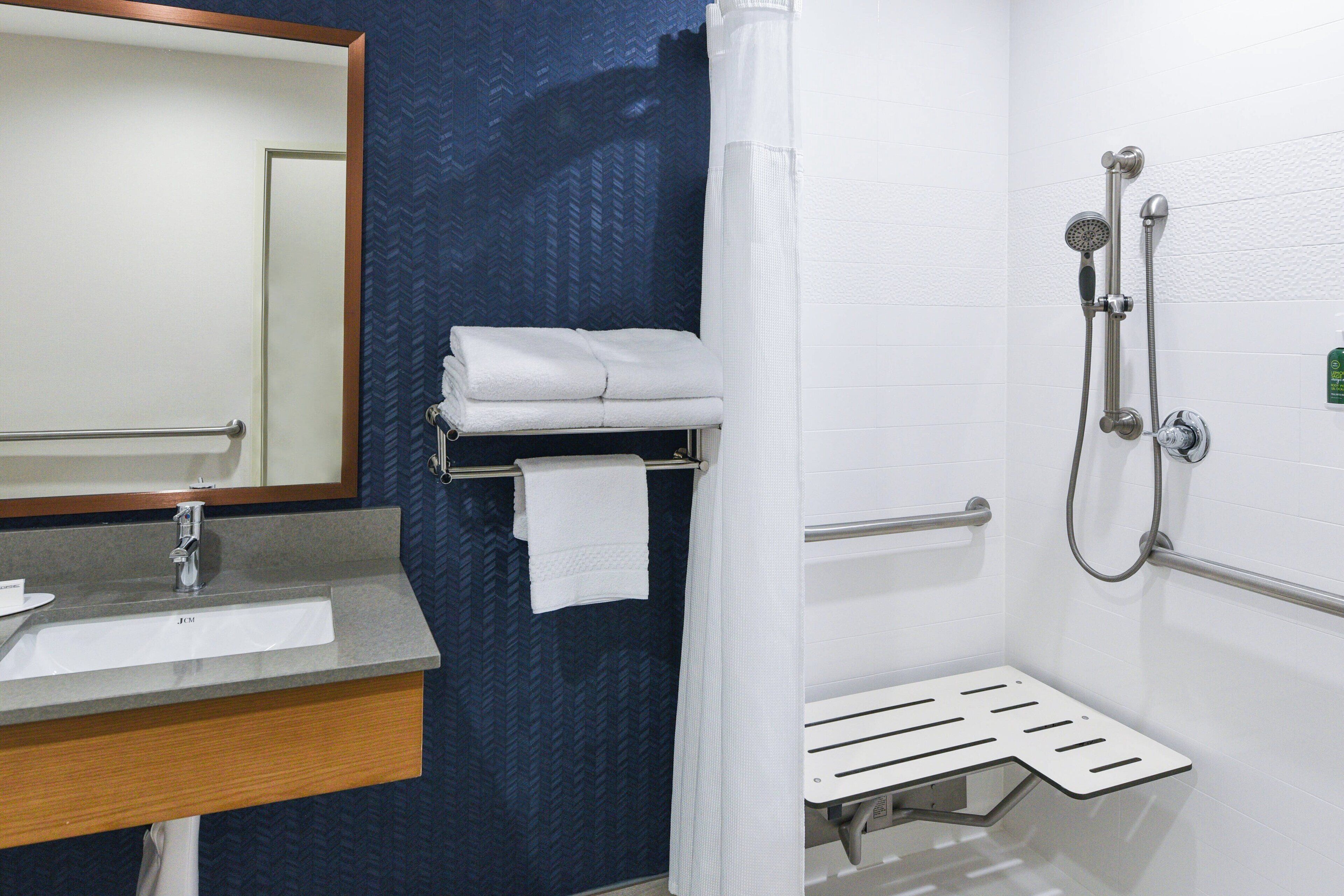 Une salle de bain équipée d’un lavabo, d’un miroir, d’un porte-serviettes, d’une douche avec des barres d’appui et d’une étagère de douche.