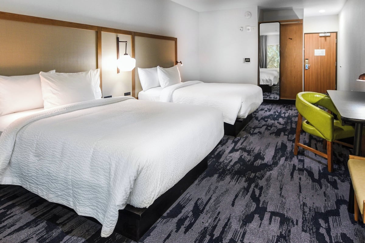 A hotel room with two beds, a desk, a chair, and a carpeted floor.
