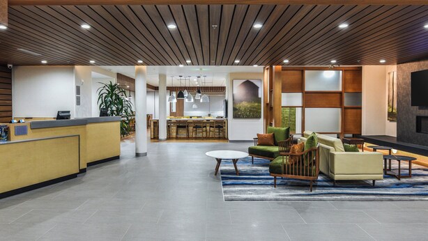 A modern lobby with a reception desk, seating area, and a kitchen in the background. - Fairfield Inn & Suites by Marriott Ontario Rancho Cucamonga (Rancho Cucamonga)