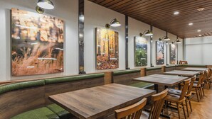 A restaurant with wooden tables and green cushioned booths, framed by large forest-themed paintings. - Fairfield Inn & Suites by Marriott Ontario Rancho Cucamonga (Rancho Cucamonga)