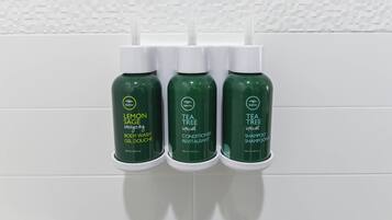 Three bottles of tea tree hair products on a white tiled wall.