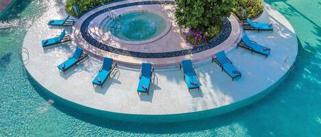 An aerial view of a resort with a circular pool surrounded by lounge chairs and a small island with a hot tub.