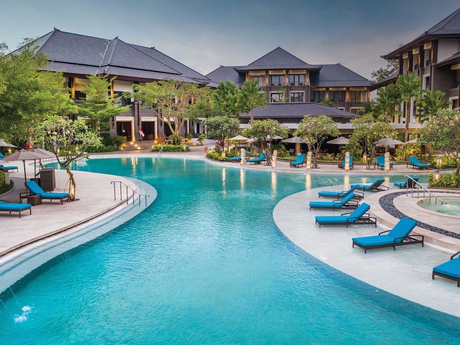 A resort with a large swimming pool, lounge areas, and multiple buildings with dark roofs.