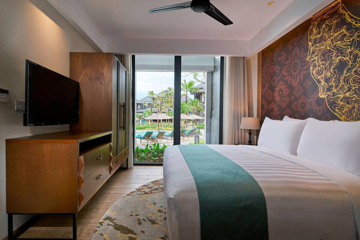 Une chambre d’hôtel équipée d’un lit, d’une télévision, d’une armoire en bois et offrant une vue sur l’espace extérieur de la piscine.