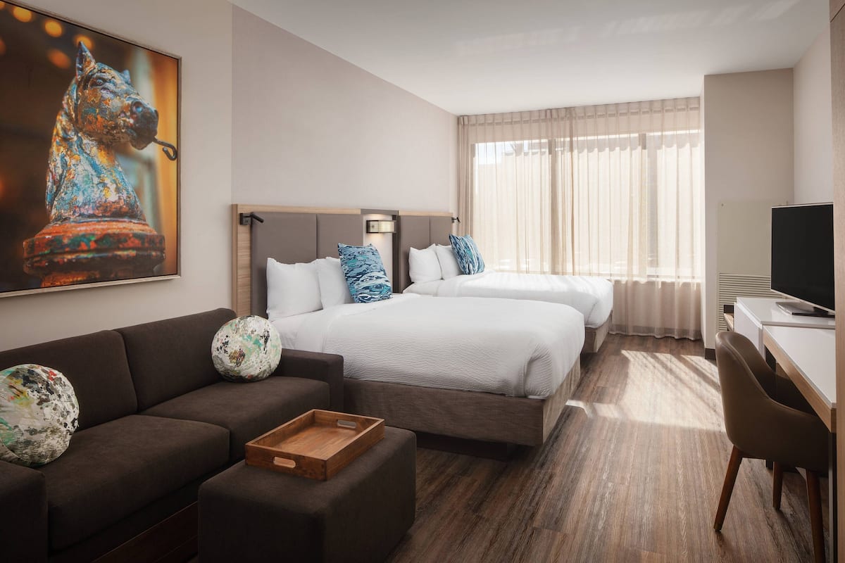 A hotel room with two beds, a sofa, a desk, and a TV.