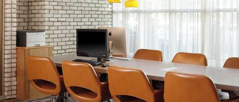 A conference room with a brick wall, a long table, six brown chairs, a computer, and yellow pendant lights.