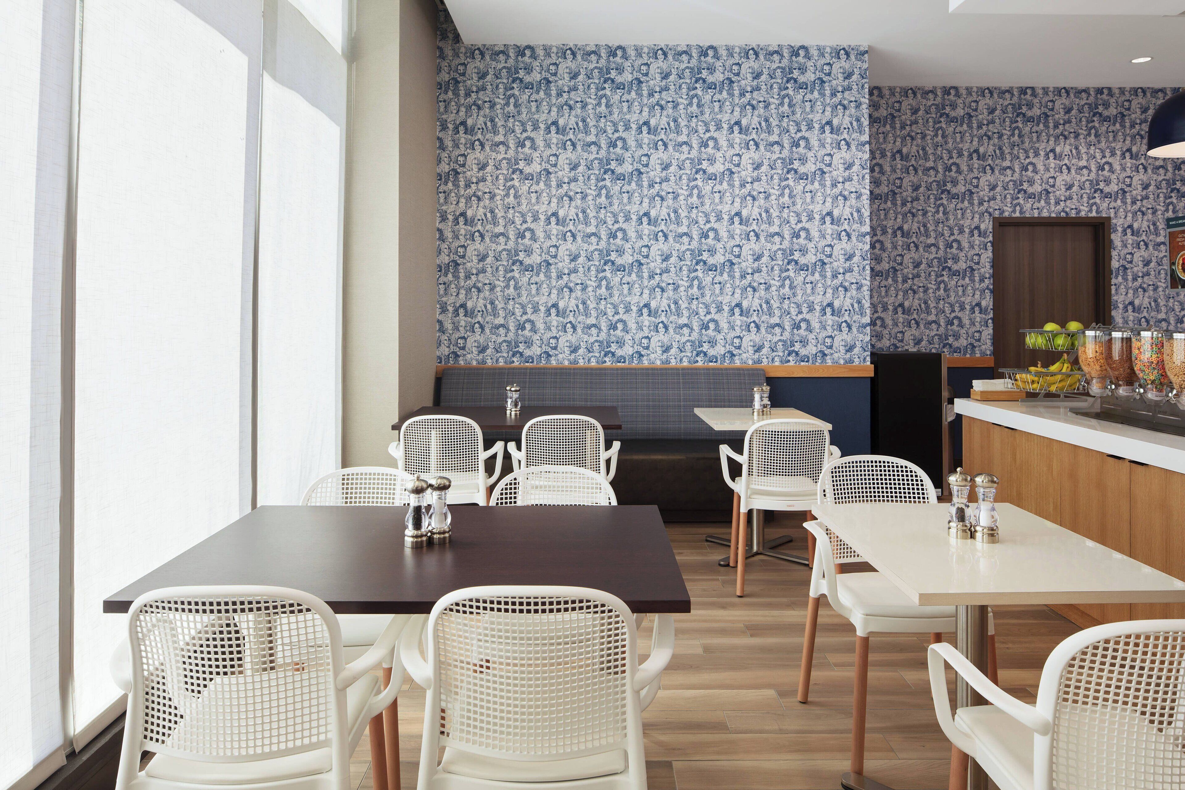 A dining area with white chairs and tables, a patterned wall, and a counter with food items.