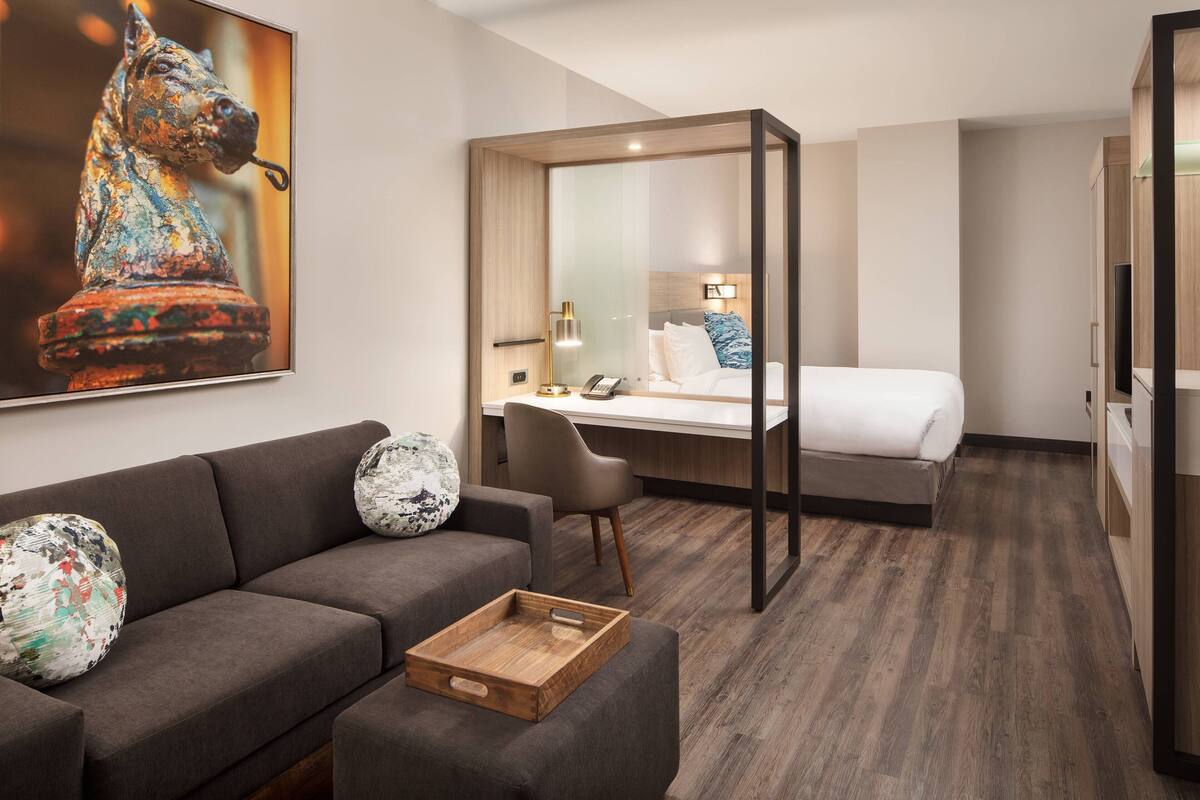 A modern hotel room with a sofa, a desk, a bed, and a large mirror.