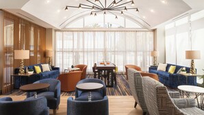 A modern hotel lobby with a central seating area, a dining table, and a large window with sheer curtains. - SpringHill Suites by Marriott New Orleans Downtown/Canal Street (New Orleans)