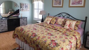 Une chambre à coucher comprenant un lit, une commode, un miroir, une lampe et des œuvres d’art accrochées aux murs.