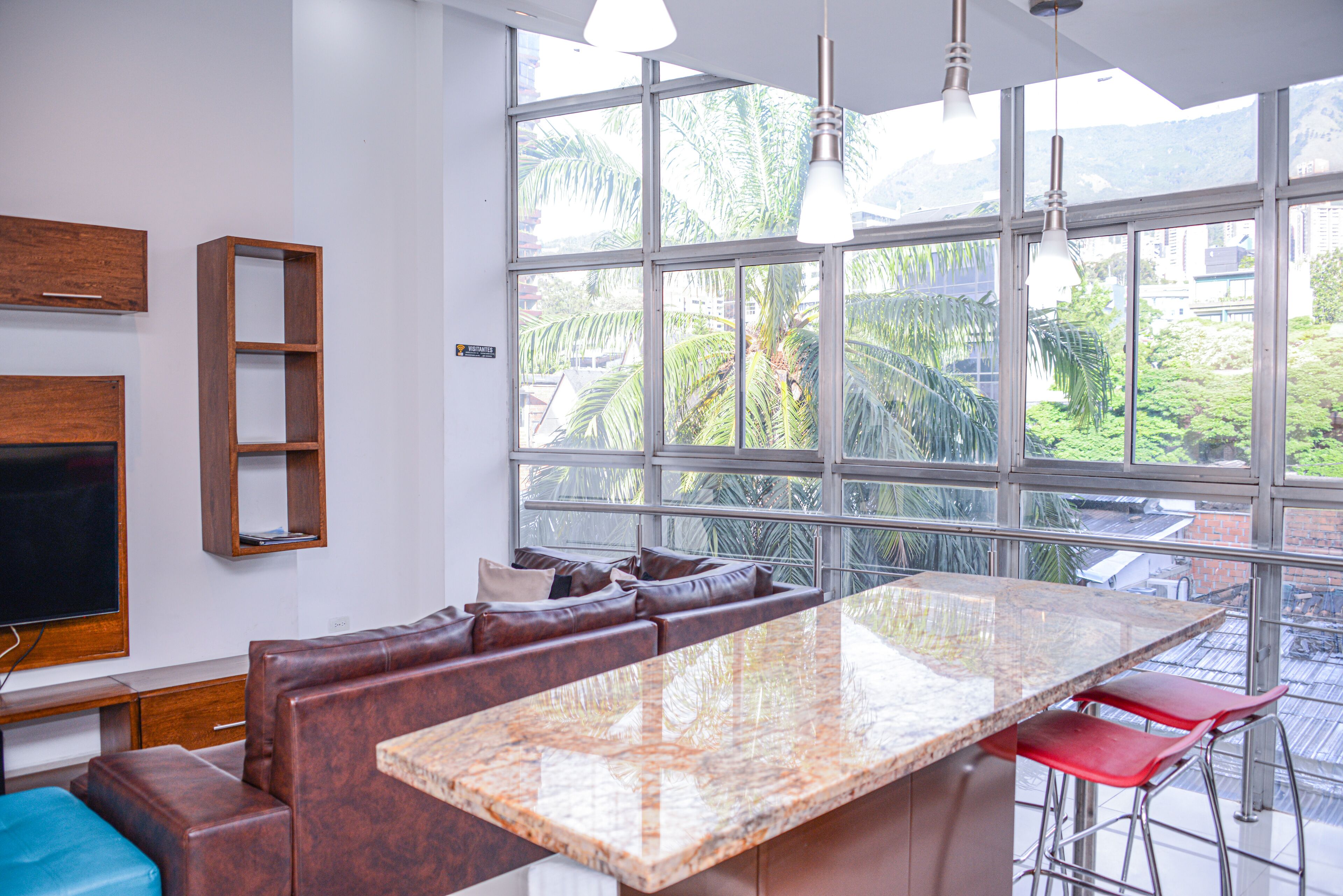 A modern kitchen with a large island, seating area, and large windows offering a view of greenery.
