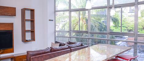 A modern kitchen with a large island, seating area, and large windows offering a view of greenery.
