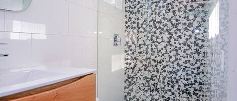 A modern bathroom with a white sink, wooden vanity, and a shower with a black and white patterned glass door.