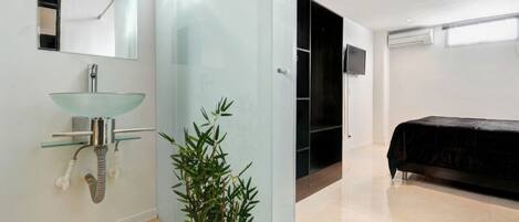 Un baño moderno con lavabo de vidrio, un espejo y una planta de bambú.