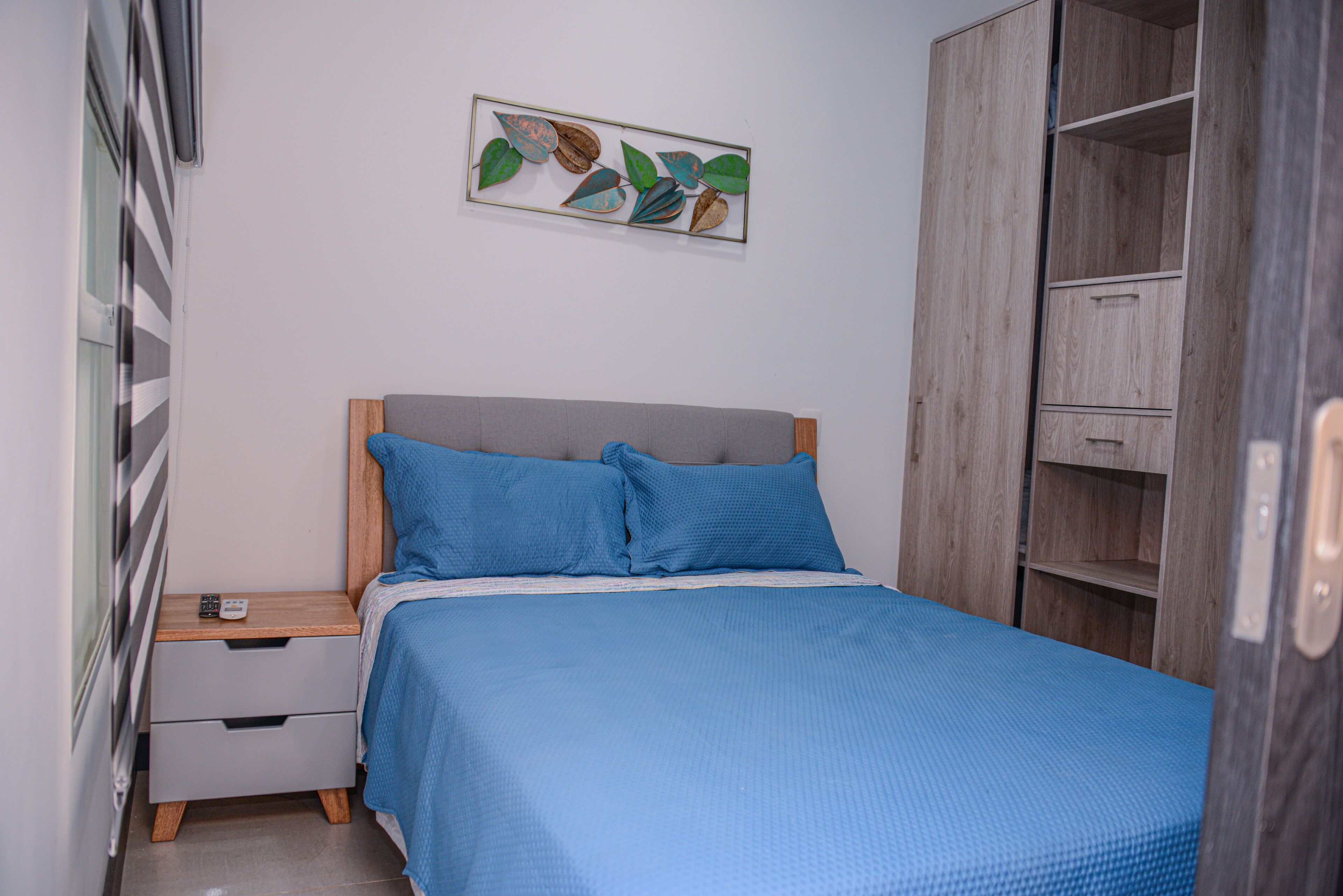 A bedroom with a bed, a nightstand, a wardrobe, and a wall art piece.