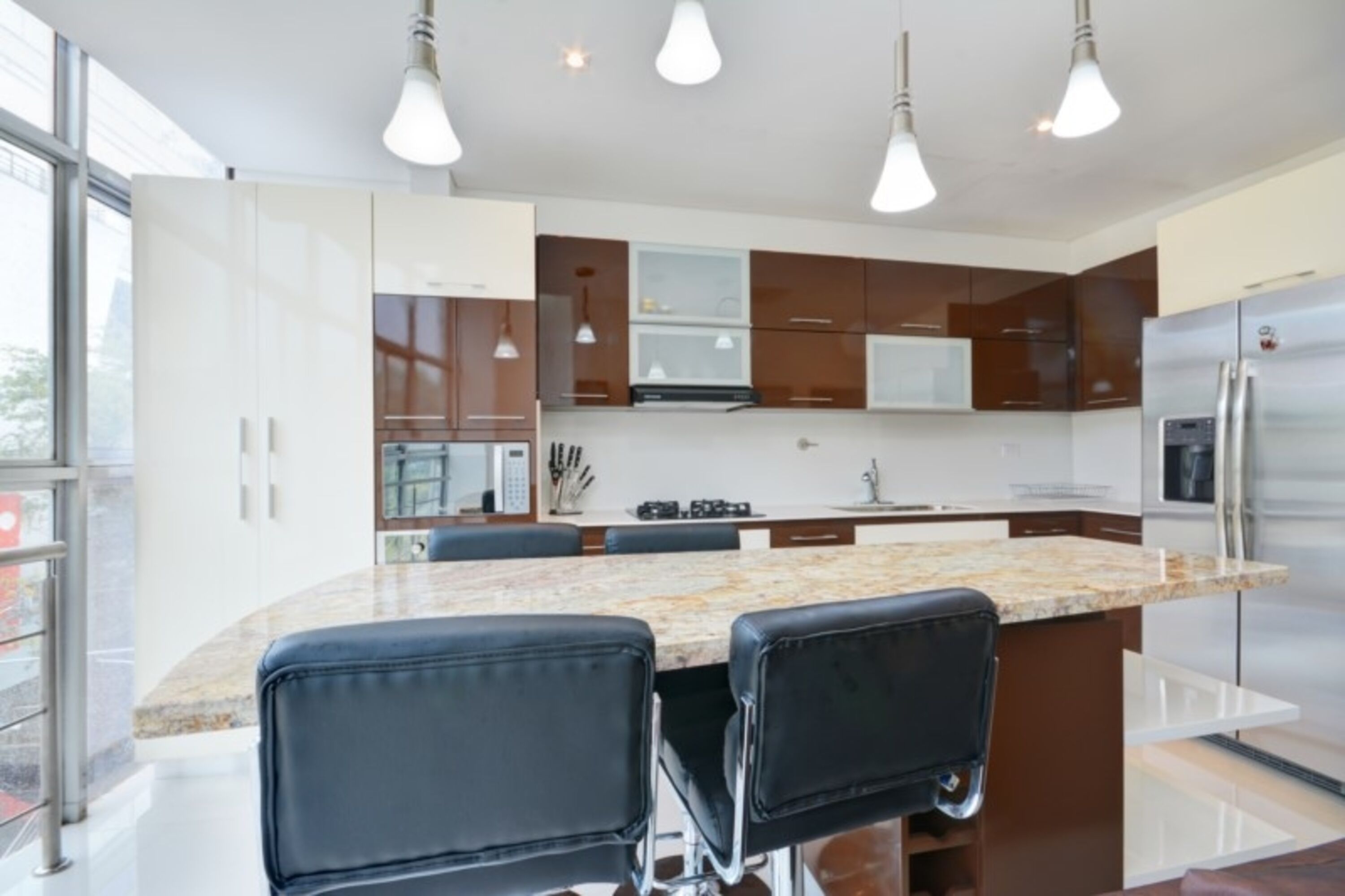 A modern kitchen with a marble countertop, stainless steel appliances, and black leather chairs.