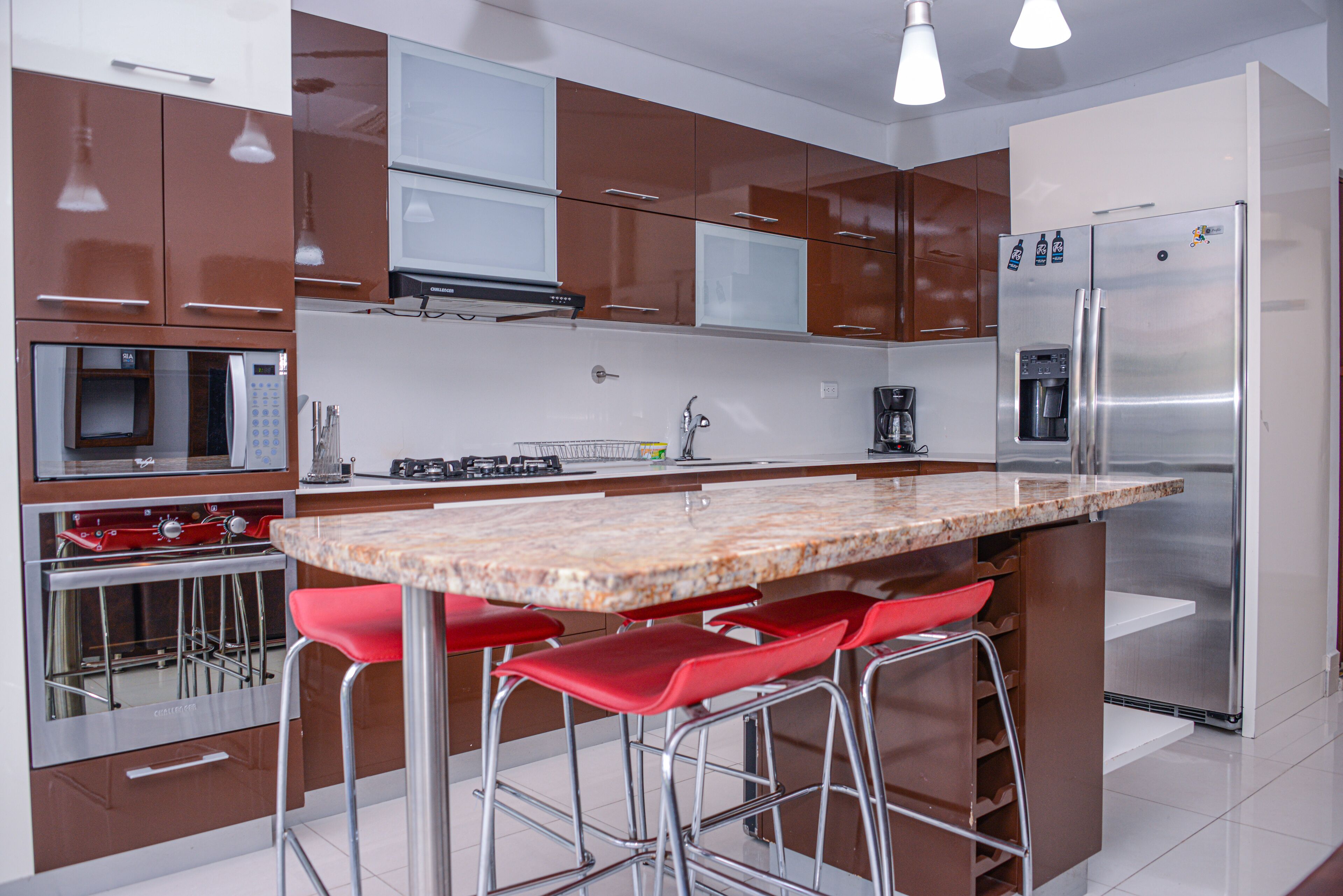 A modern kitchen with stainless steel appliances, a marble countertop, and red bar stools.