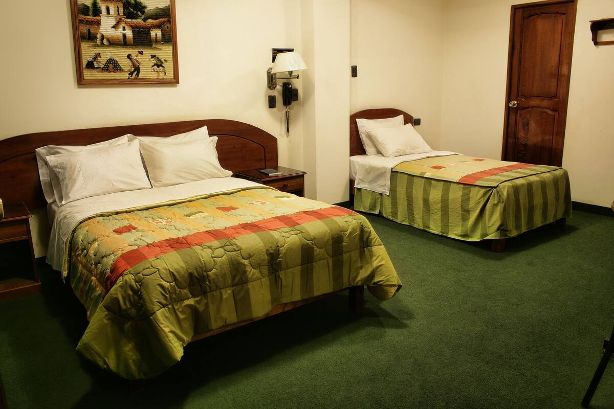 A hotel room with two single beds, a nightstand, a lamp, and a painting on the wall.