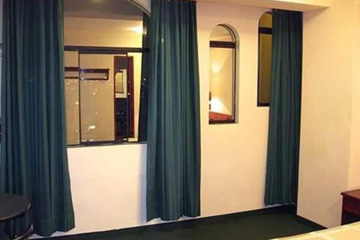 A hotel room with a bed, a desk, a chair, and a mirror.