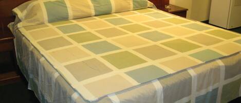 Un letto rifatto con una coperta a quadri in tonalità neutre, una testiera in legno e un comodino con una lampada.