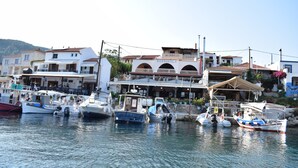 A marina with several boats docked, a building with a sign reading "SOSSINOLA", and a hillside in the background.