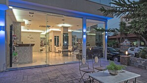 Un hotel moderno con fachada de vidrio, zona de estar al aire libre y un interior visible que incluye una recepción.