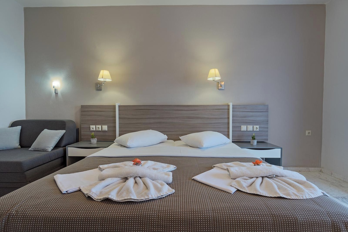 A hotel room with a large bed, two bedside tables, a sofa, and two wall-mounted lamps.