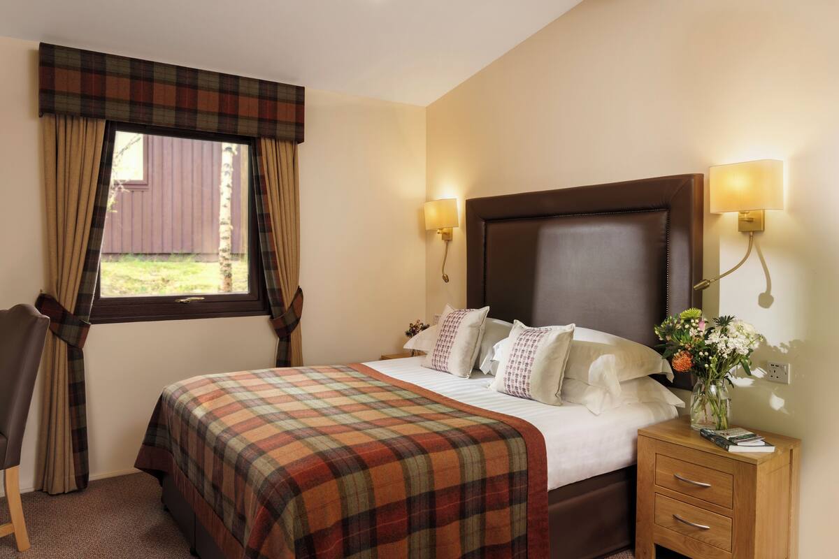 A hotel room with a bed, a chair, a nightstand, a lamp, and a window with curtains.