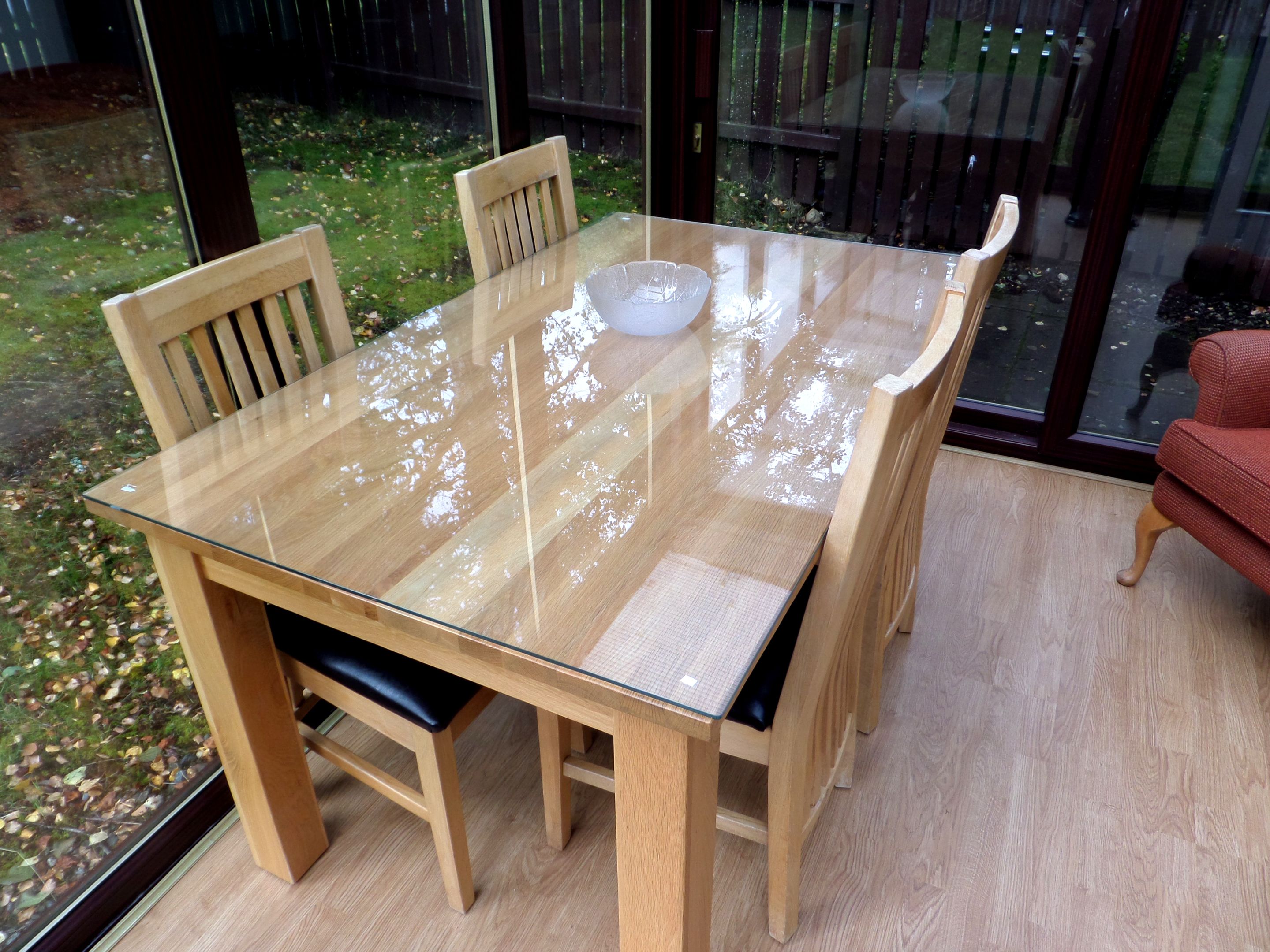 A glass-top dining table with four wooden chairs, a bowl, and a red chair in the background.