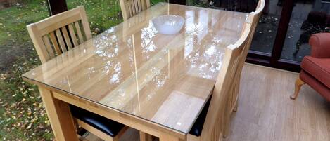 Una mesa de vidrio para comedor con cuatro sillas de madera, un cuenco y una silla roja al fondo.