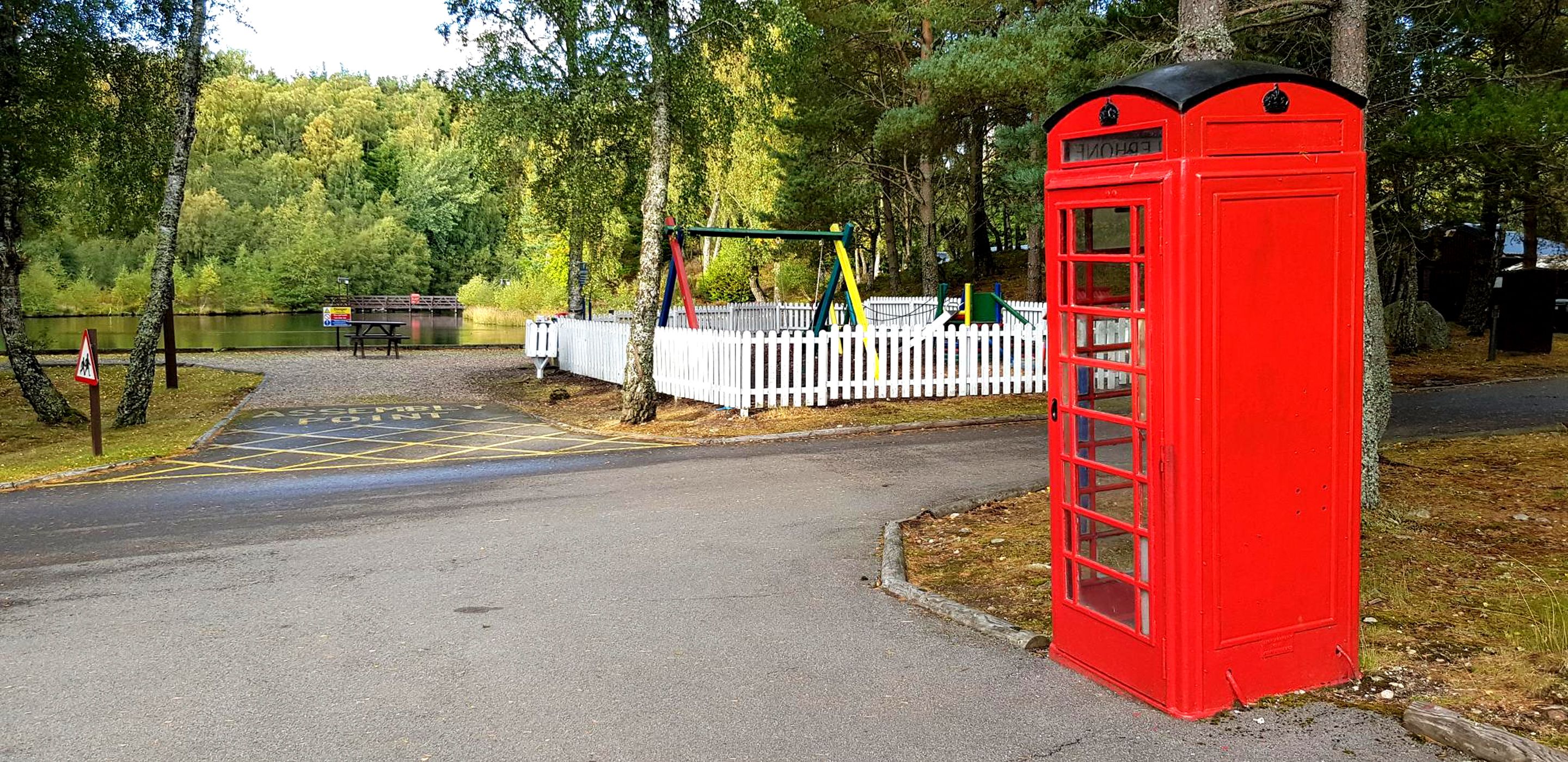 Une cabine téléphonique rouge, une aire de jeux et une vue sur un lac.