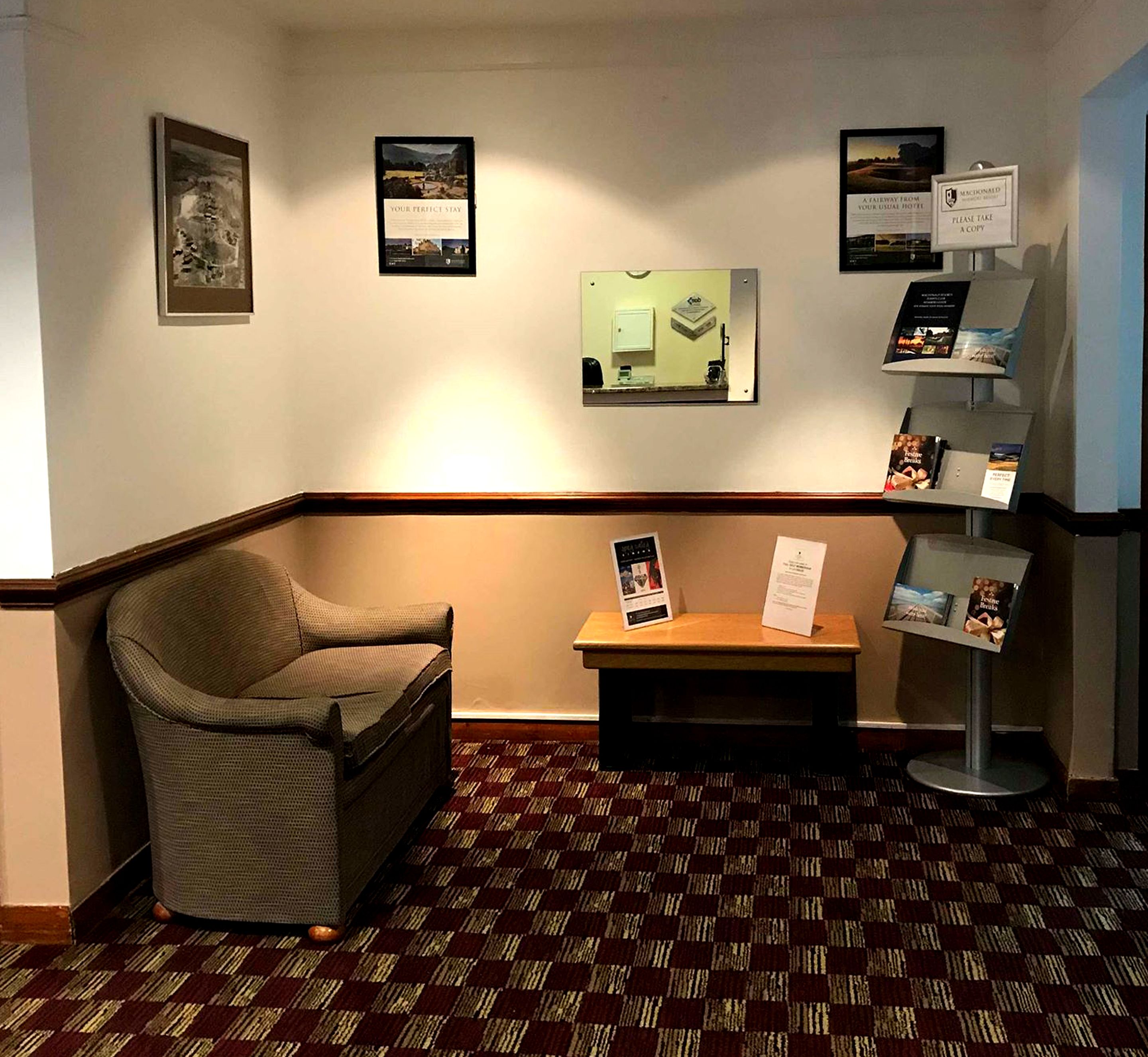 A hotel lobby with a check-in desk, a seating area with a chair, and informational posters on the walls.