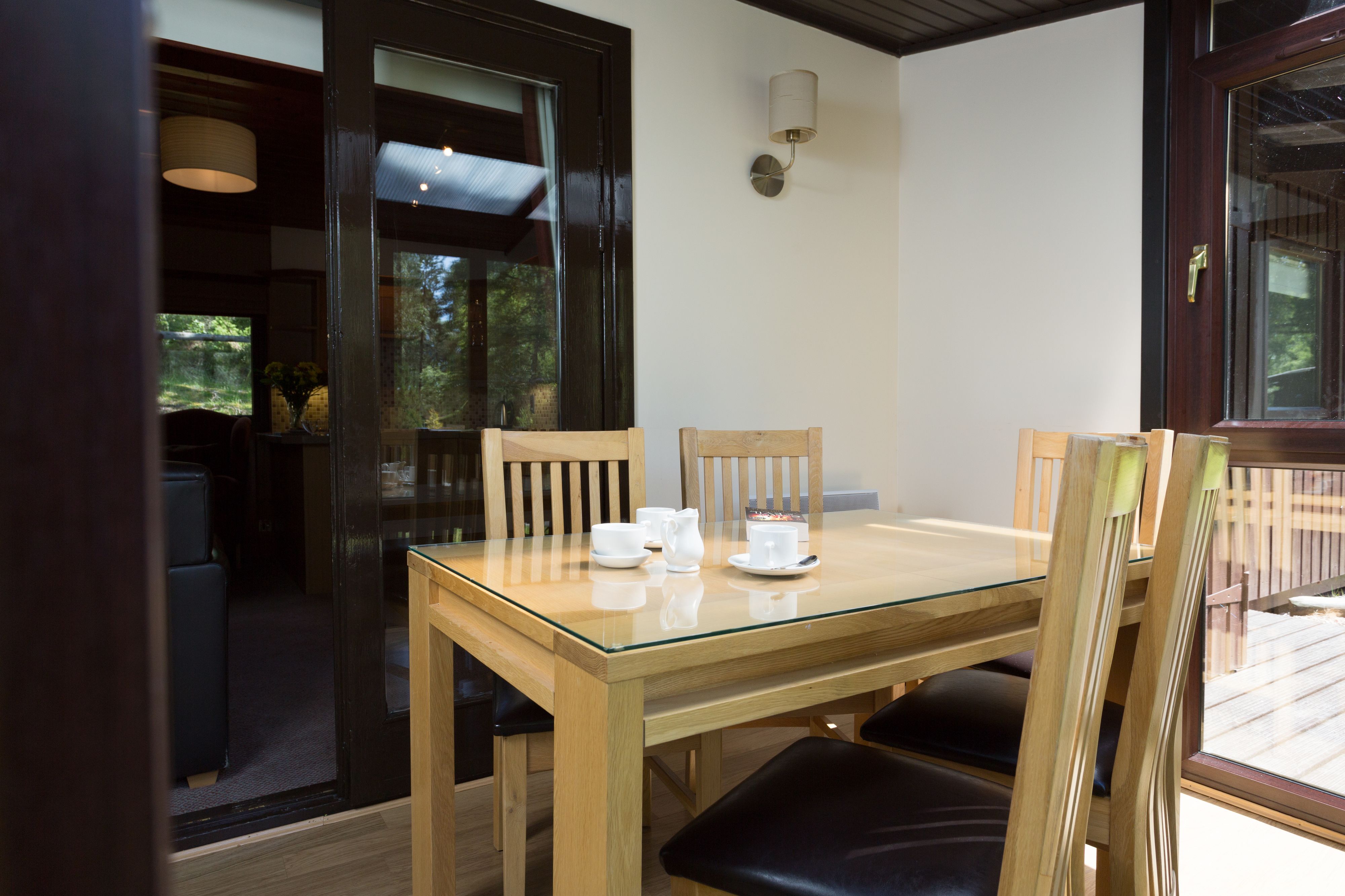 Un coin repas avec une table à plateau en verre, des chaises en bois, ainsi qu’un pichet et des tasses blancs.
