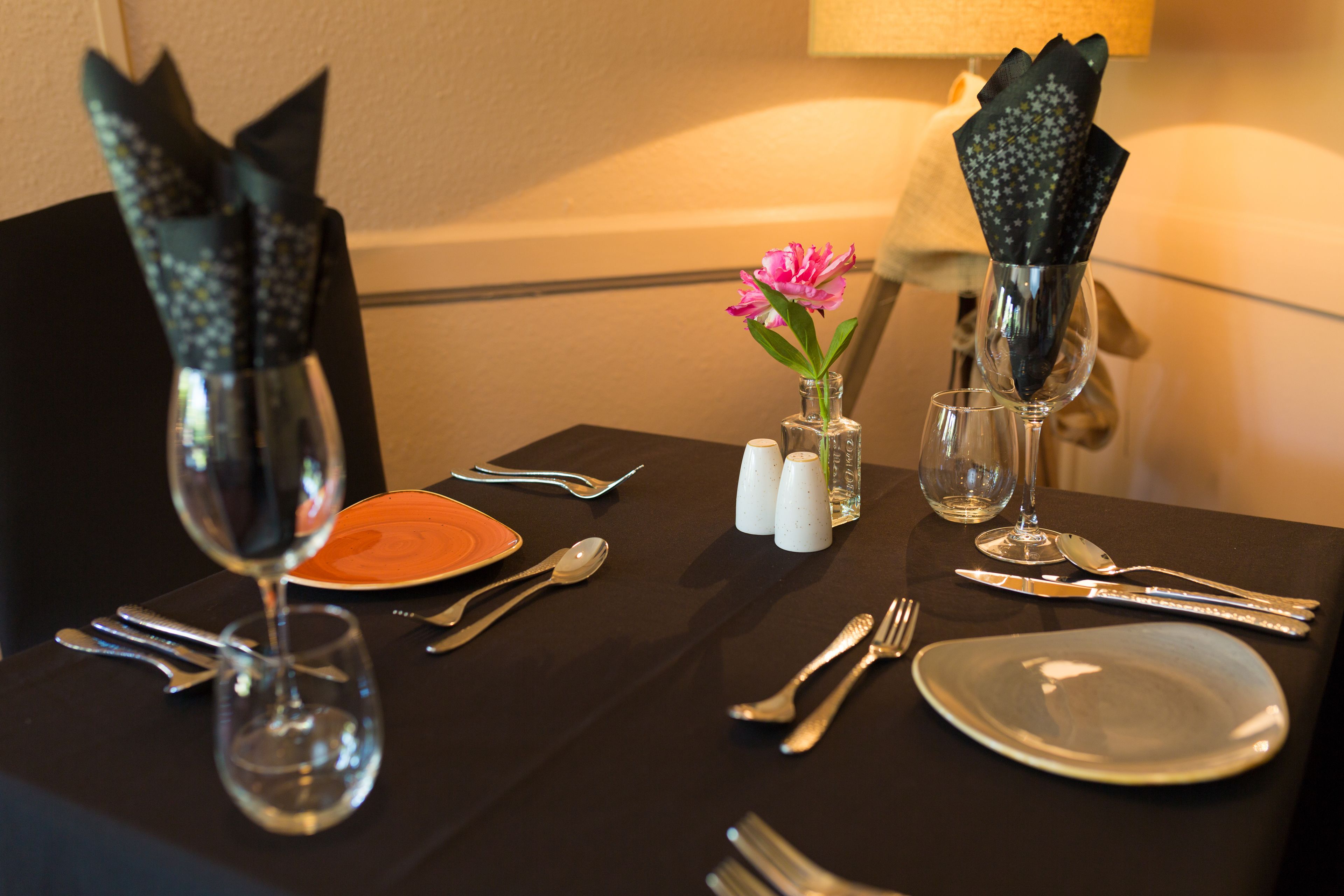 A table set with dinnerware, cutlery, and a vase with a flower.