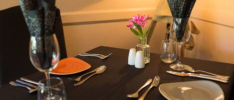 A table set with dinnerware, cutlery, and a vase with a flower.